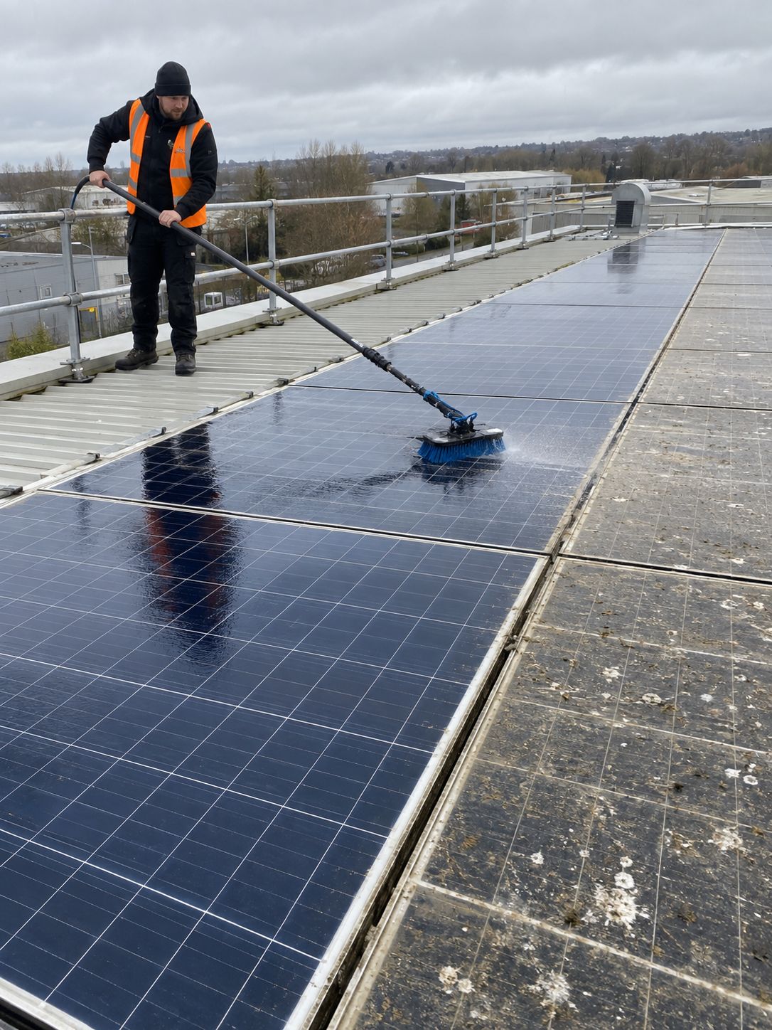 Cleaning a commercial rooftop solar array with a water-fed brush, clean panels next to dirty ones